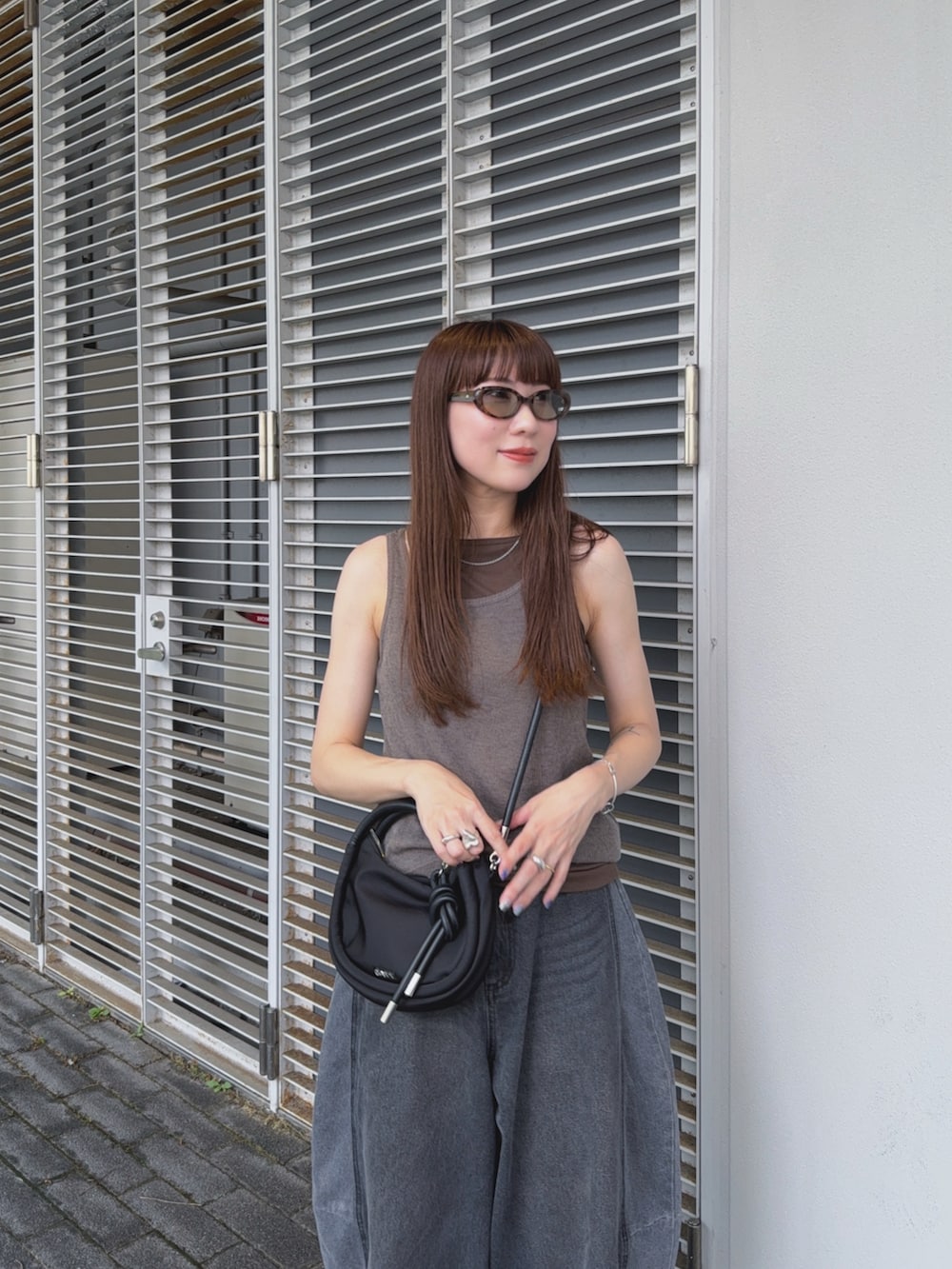 グレー系のタンクトップ、ブラック系のデニムパンツ、ブラック系のショルダーバッグを着用したレディースの夏コーディネートの4枚目の写真