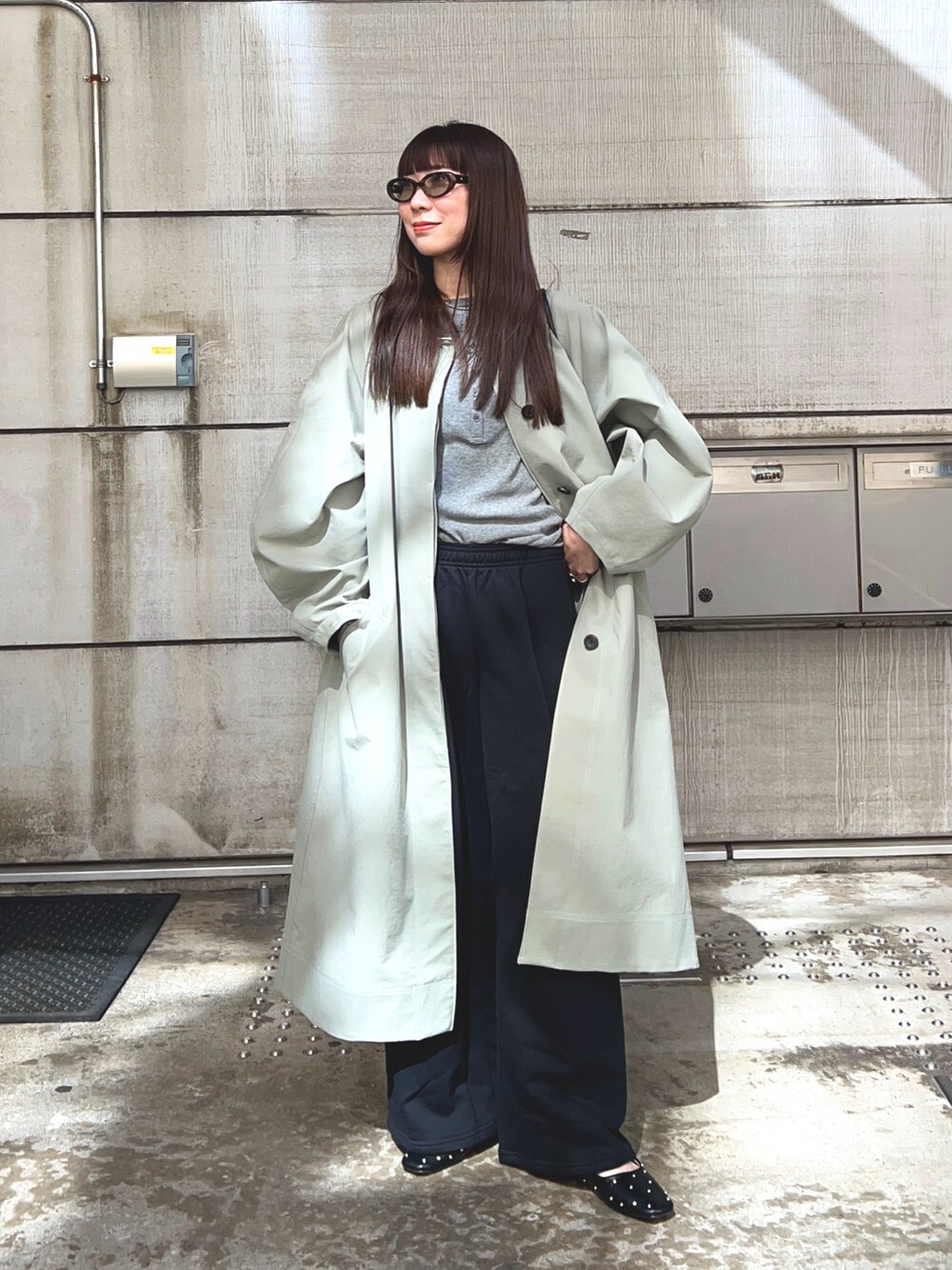 グリーン系のステンカラーコート、グレー系のTシャツ/カットソー、ブラック系のスウェットパンツを着用したレディースの春コーディネートの2枚目の写真