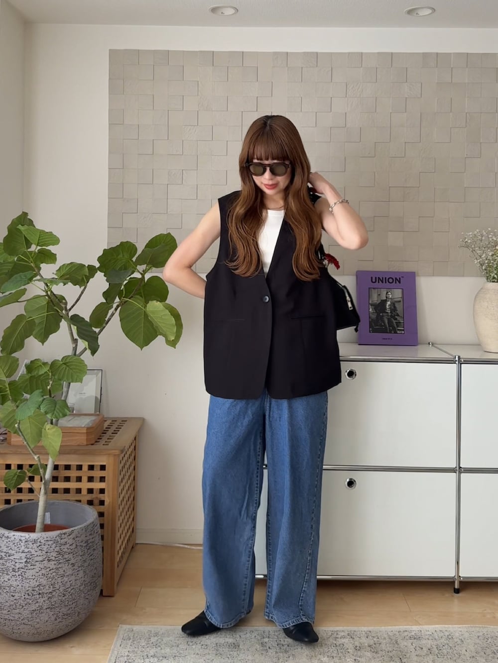 ブラック系のベスト、ブルー系のデニムパンツ、ブラック系のスリッポンを着用したレディースの春コーディネートの3枚目の写真