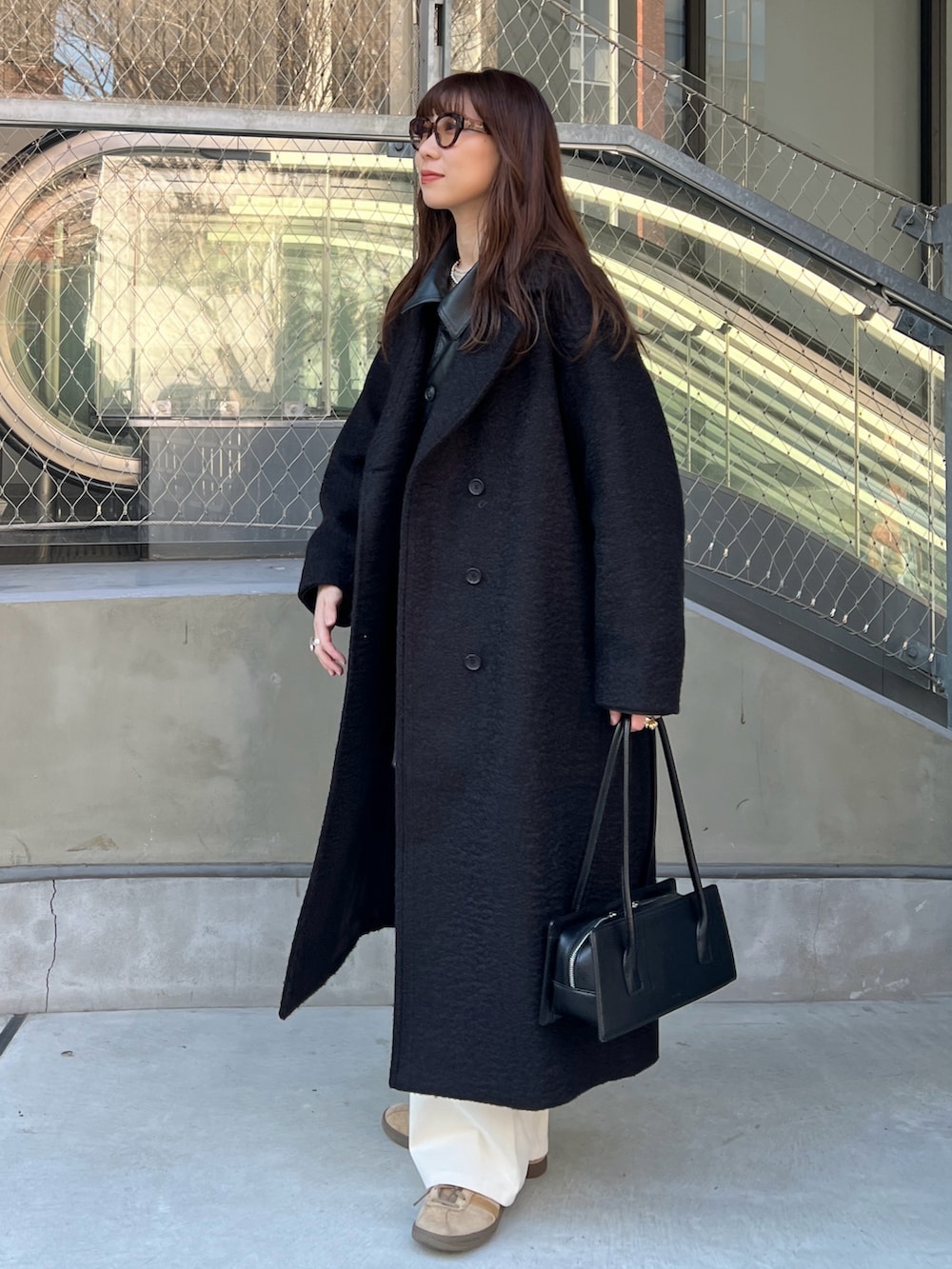 ブラック系のステンカラーコート、ブラック系のその他アウター、ホワイト系のニット/セーターを着用したレディースの冬コーディネートの2枚目の写真