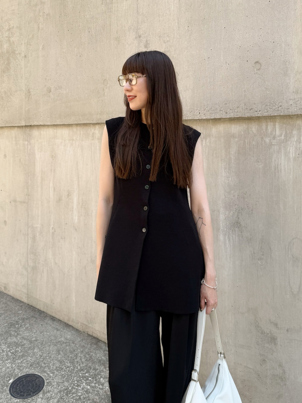 ブラック系のベスト、ブラック系のスラックス、ホワイト系のバッグを着用したレディースの夏コーディネートの4枚目の写真