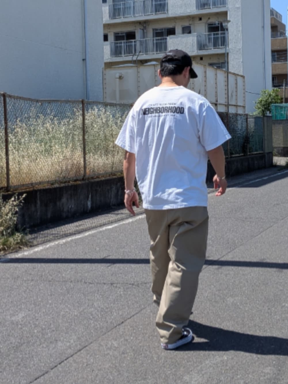 ホワイト系のTシャツ/カットソー、ベージュ系のチノパンツ、ブラック系のスニーカーを着用したメンズの夏コーディネートの2枚目の写真