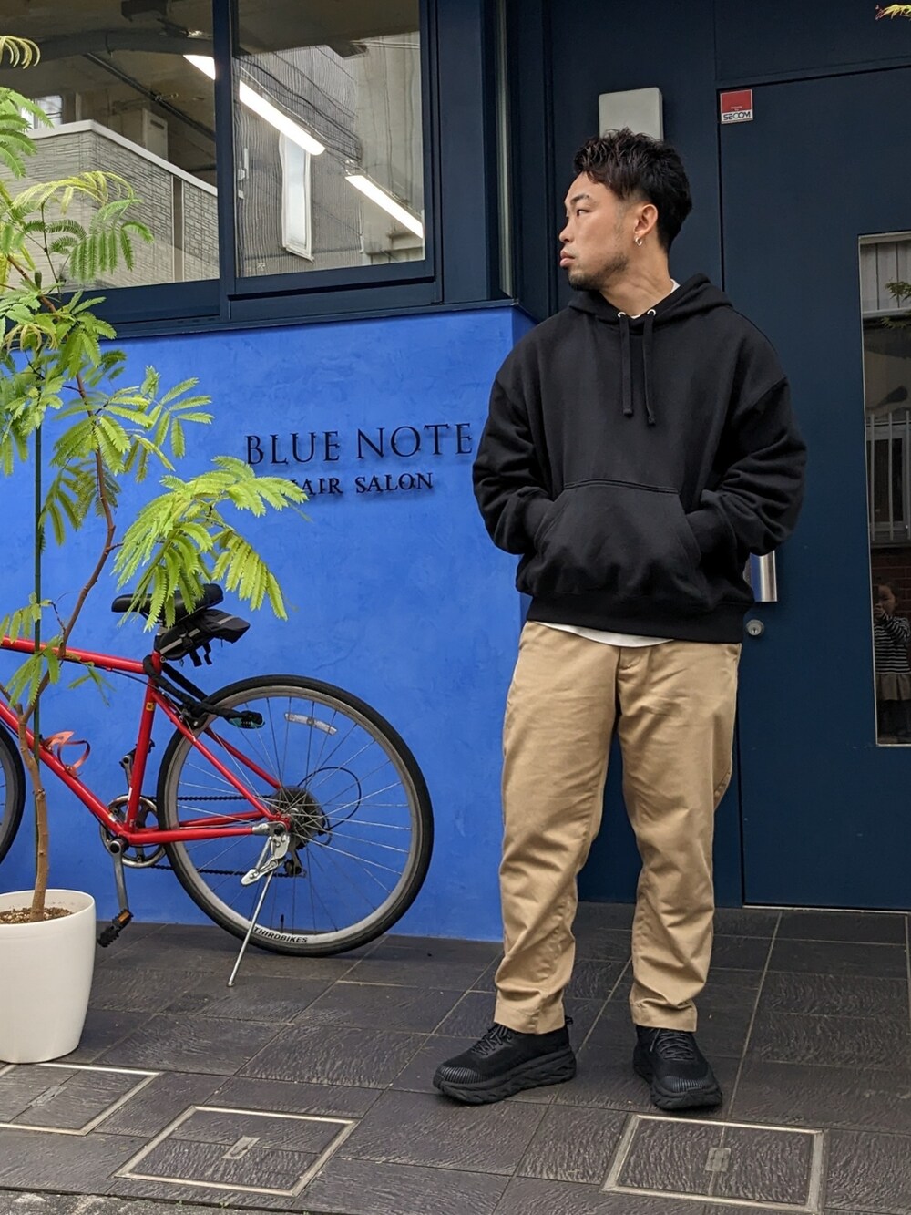 ブラック系のパーカー、ベージュ系のチノパンツ、ブラック系のスニーカーを着用したメンズの春コーディネートの2枚目の写真