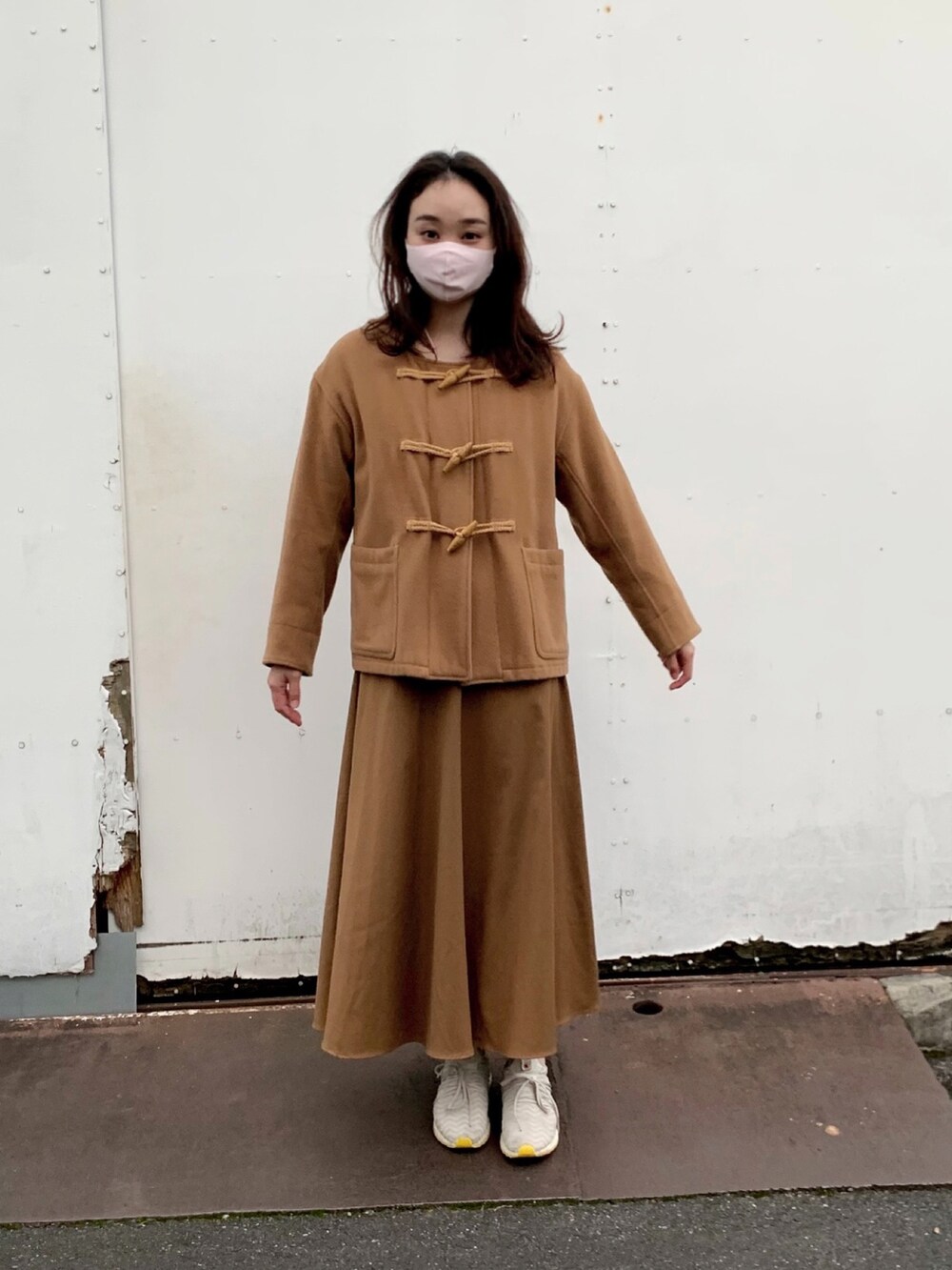 ベージュ系のダッフルコート、ブラウン系のスカート、グレー系のスニーカーを着用したレディースの秋コーディネートの2枚目の写真
