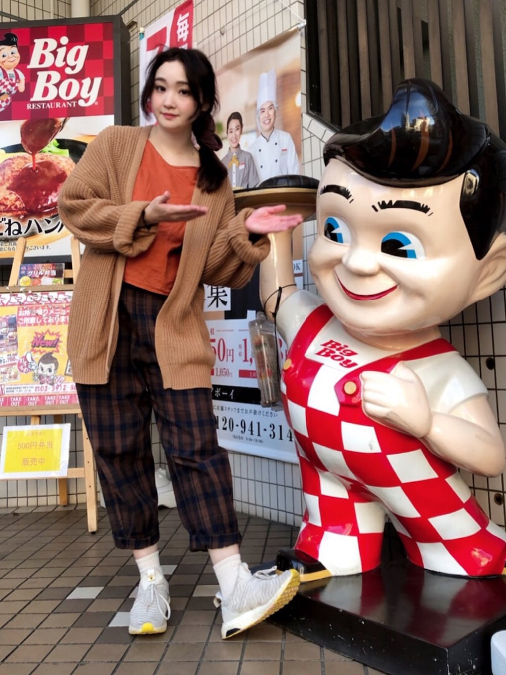 オレンジ系のシャツ/ブラウス、ブラウン系のカーディガン/ボレロ、ブラウン系のパンツを着用したレディースの秋コーディネートの2枚目の写真