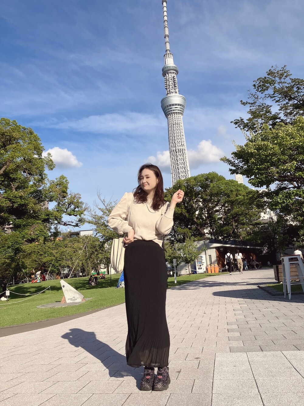 ベージュ系のTシャツ/カットソー、ブラック系のスカート、ブラック系のスニーカーを着用したレディースの秋コーディネートの2枚目の写真