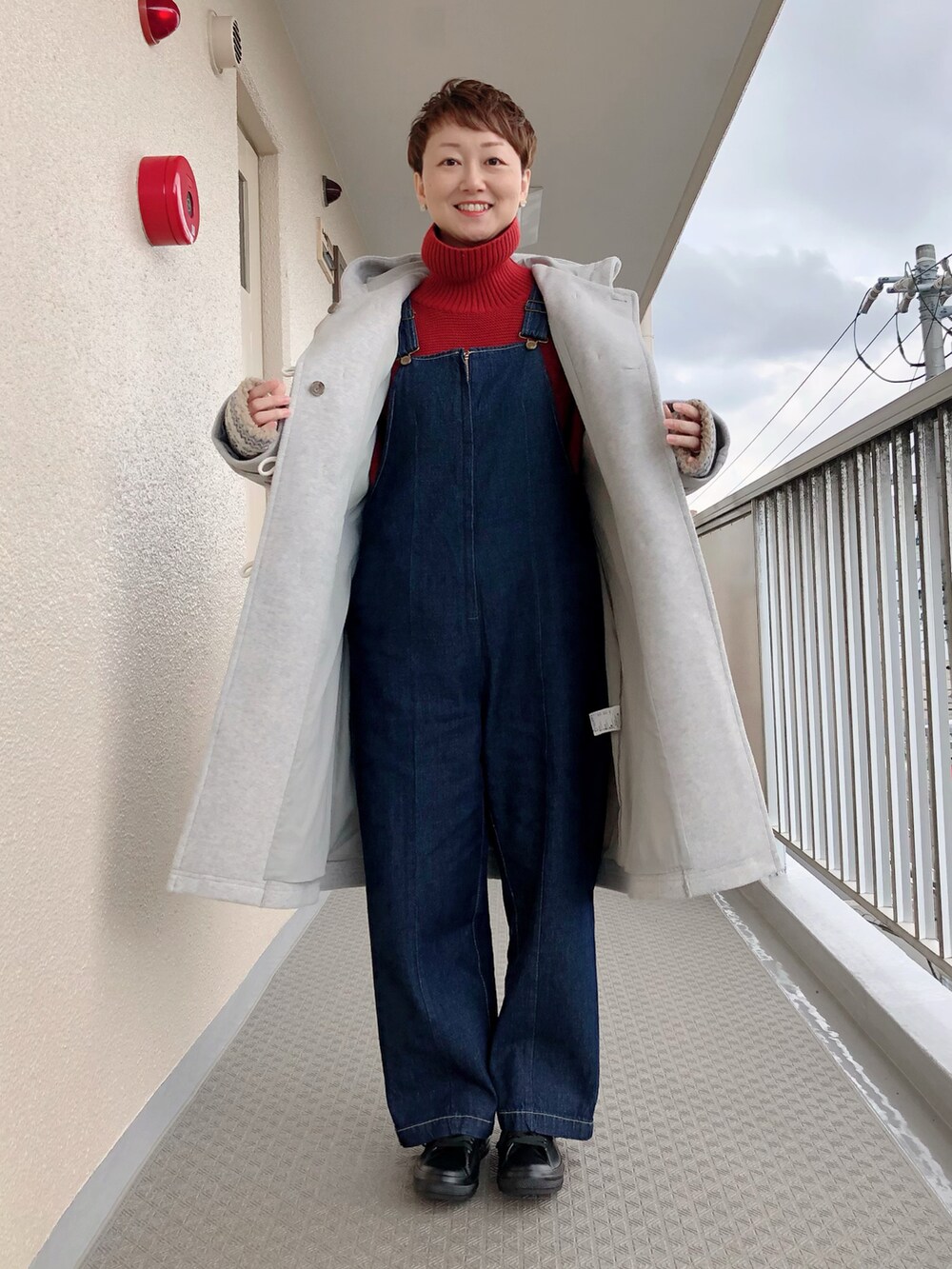 グレー系のダッフルコート、ブルー系のサロペット/オーバーオール、レッド系のニット/セーターを着用したレディースの冬コーディネートの2枚目の写真