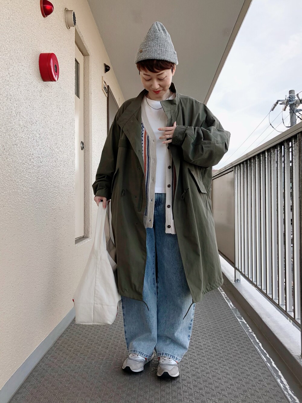 グリーン系のモッズコート、オレンジ系のカーディガン/ボレロ、ブルー系のデニムパンツを着用したレディースの冬コーディネートの2枚目の写真