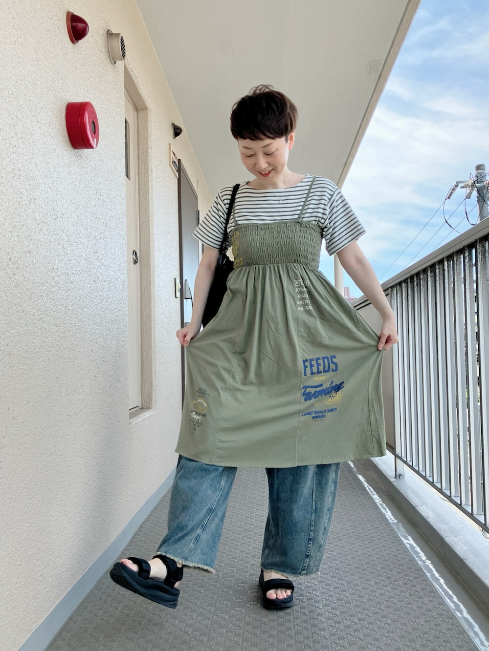 グリーン系のチュニック、ブラック系のサンダル、ブルー系のその他パンツを着用したレディースの夏コーディネートの2枚目の写真