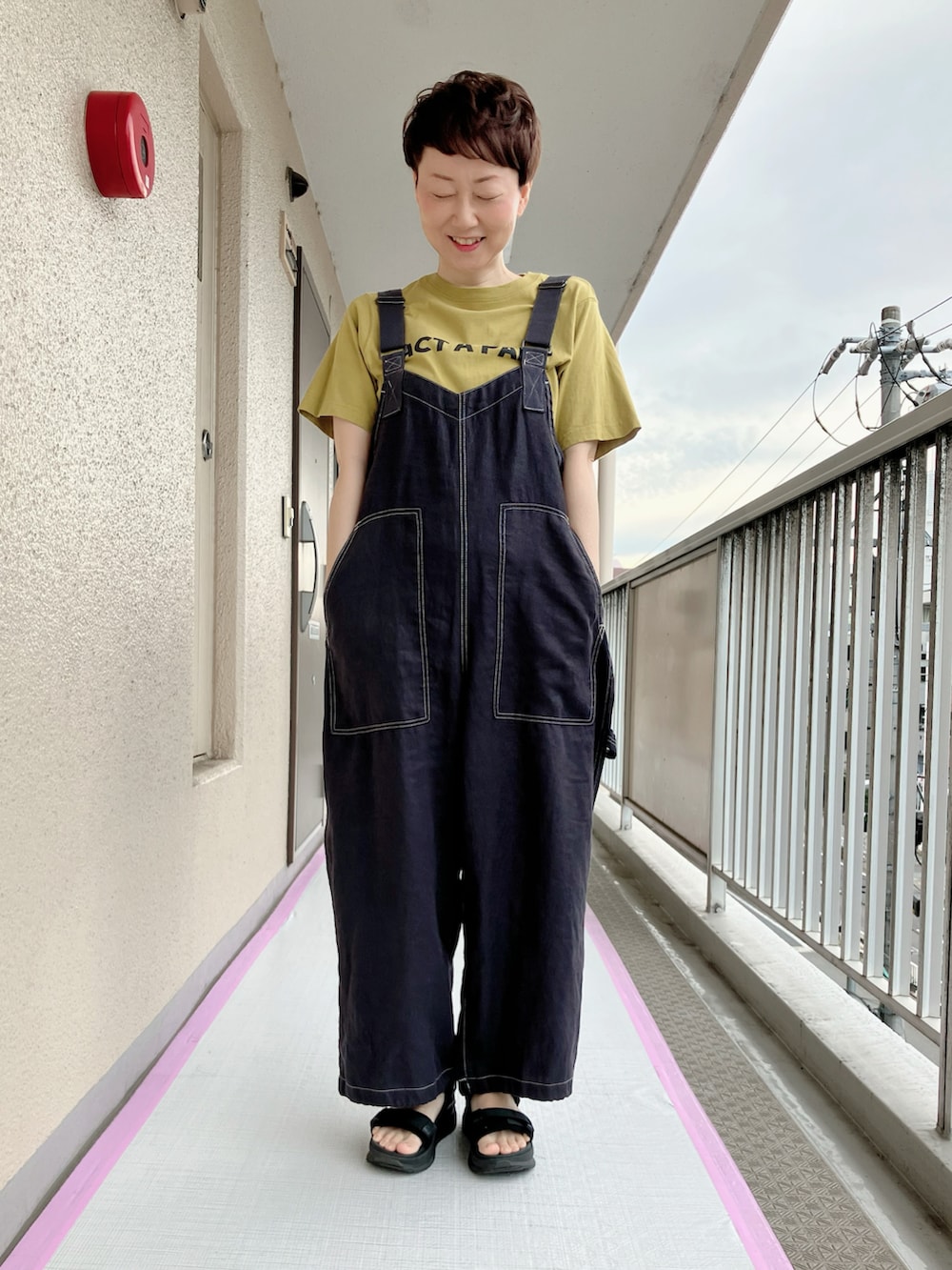 イエロー系のTシャツ/カットソー、ブラック系のサロペット/オーバーオール、ブラック系のサンダルを着用したレディースの夏コーディネートの2枚目の写真