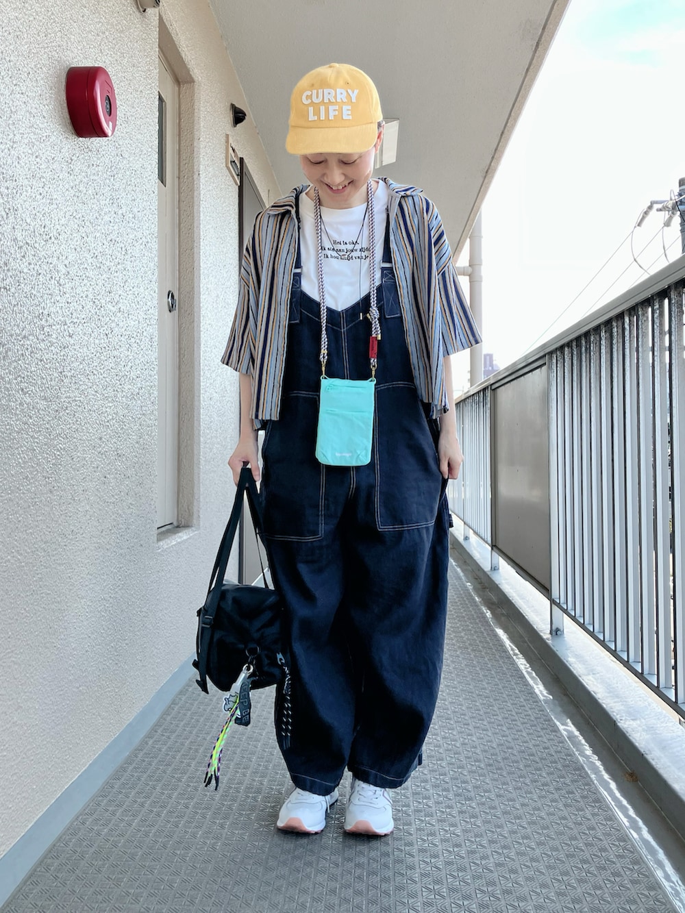 ブルー系のシャツ/ブラウス、ブラック系のサロペット/オーバーオール、イエロー系のキャップを着用したレディースの夏コーディネートの2枚目の写真