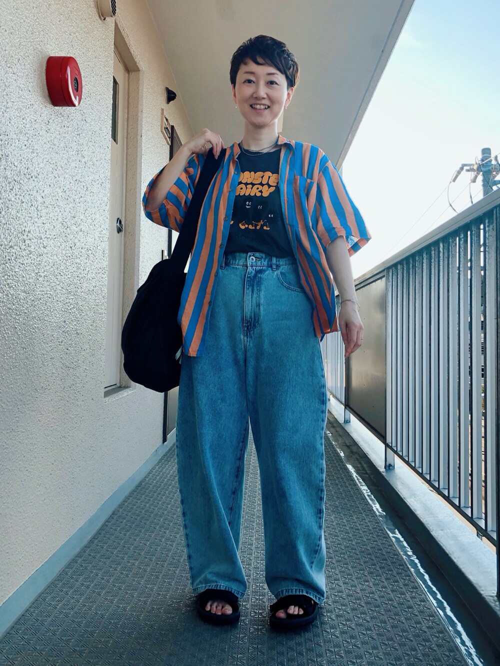 オレンジ系のシャツ/ブラウス、グレー系のTシャツ/カットソー、ブルー系のデニムパンツを着用したレディースの夏コーディネートの2枚目の写真