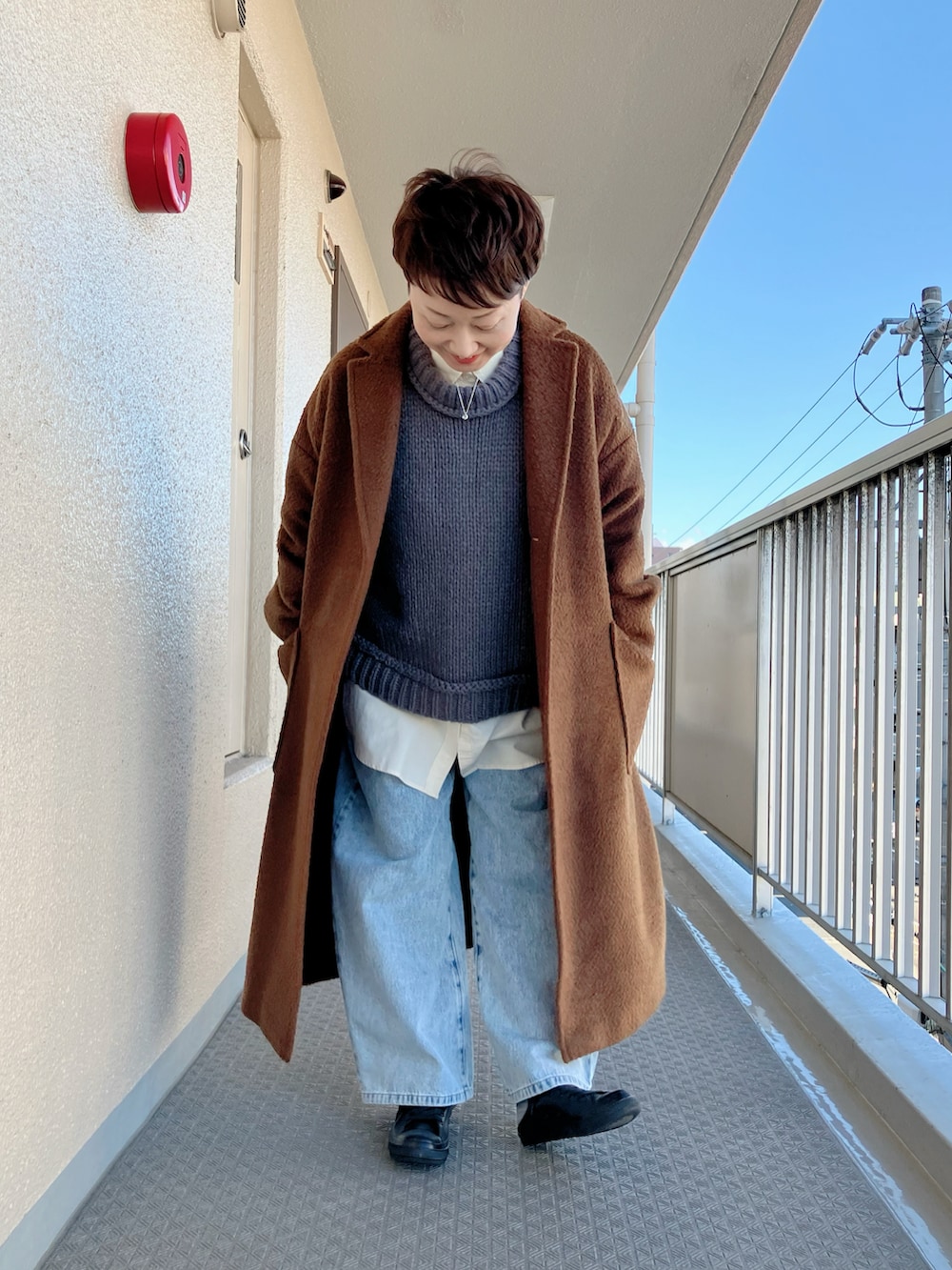 ブラウン系のチェスターコート、グレー系のニット/セーター、ブルー系のデニムパンツを着用したレディースの冬コーディネートの2枚目の写真