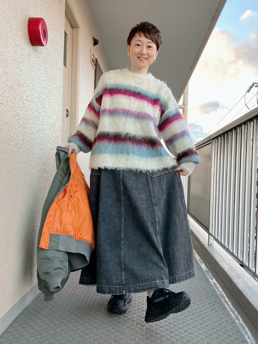 グリーン系のMA-1、ホワイト系のニット/セーター、ブラック系のデニムスカートを着用したレディースの冬コーディネートの2枚目の写真