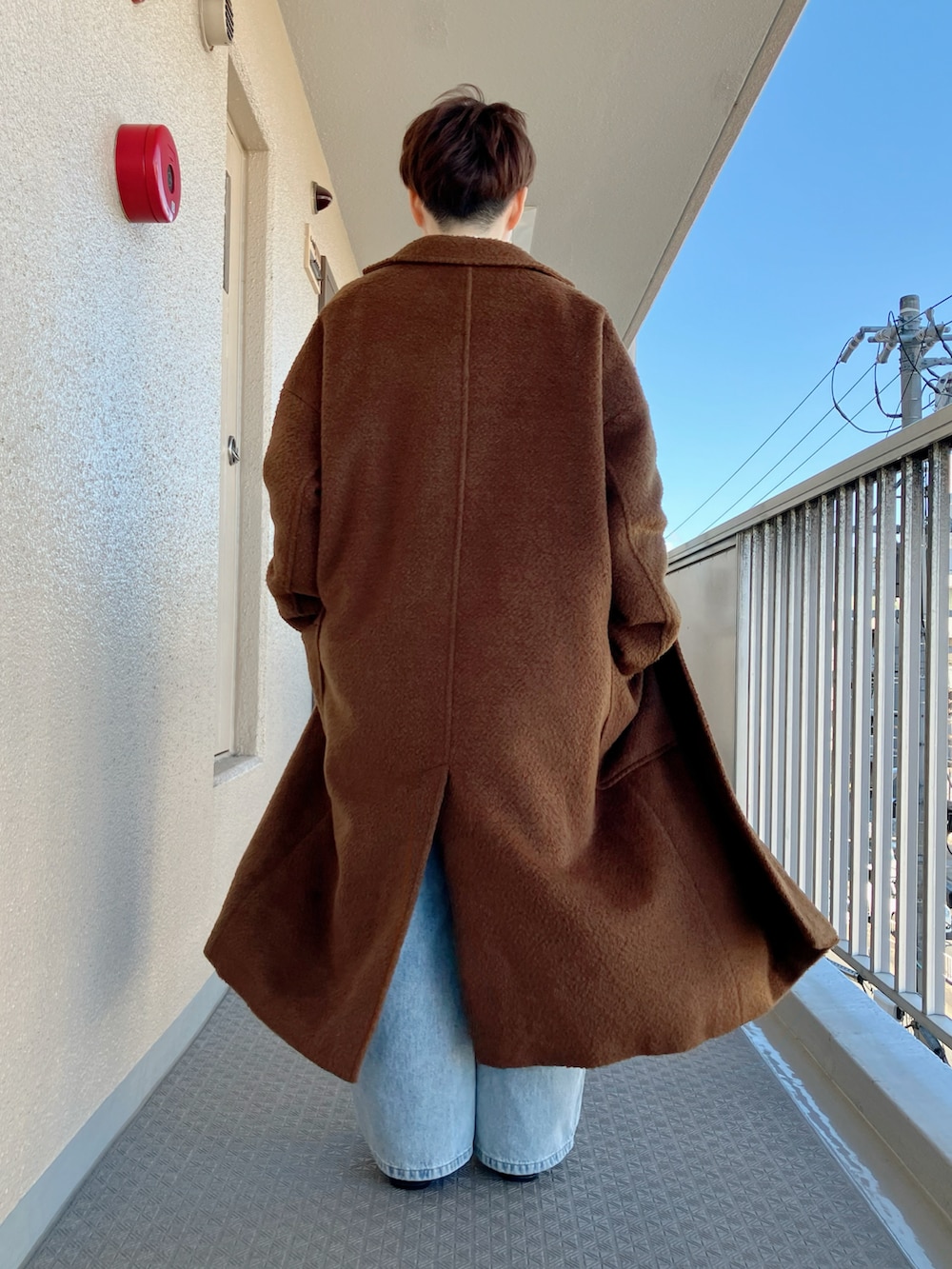 ブラウン系のチェスターコート、グレー系のニット/セーター、ブルー系のデニムパンツを着用したレディースの冬コーディネートの3枚目の写真