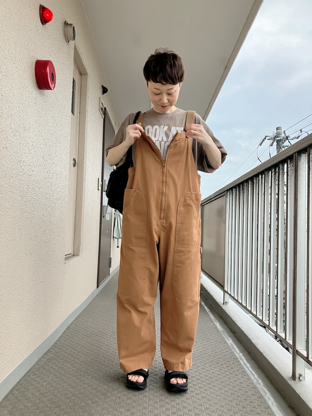 ベージュ系のTシャツ/カットソー、イエロー系のサロペット/オーバーオール、ブラック系のサンダルを着用したレディースの夏コーディネートの2枚目の写真