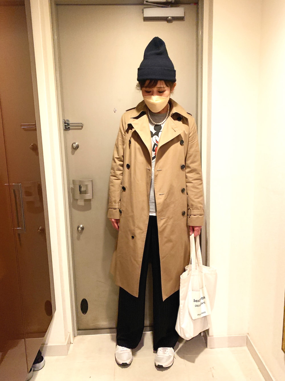 ベージュ系のトレンチコート、ブラック系のスラックス、ホワイト系のトートバッグを着用したレディースの春コーディネートの2枚目の写真