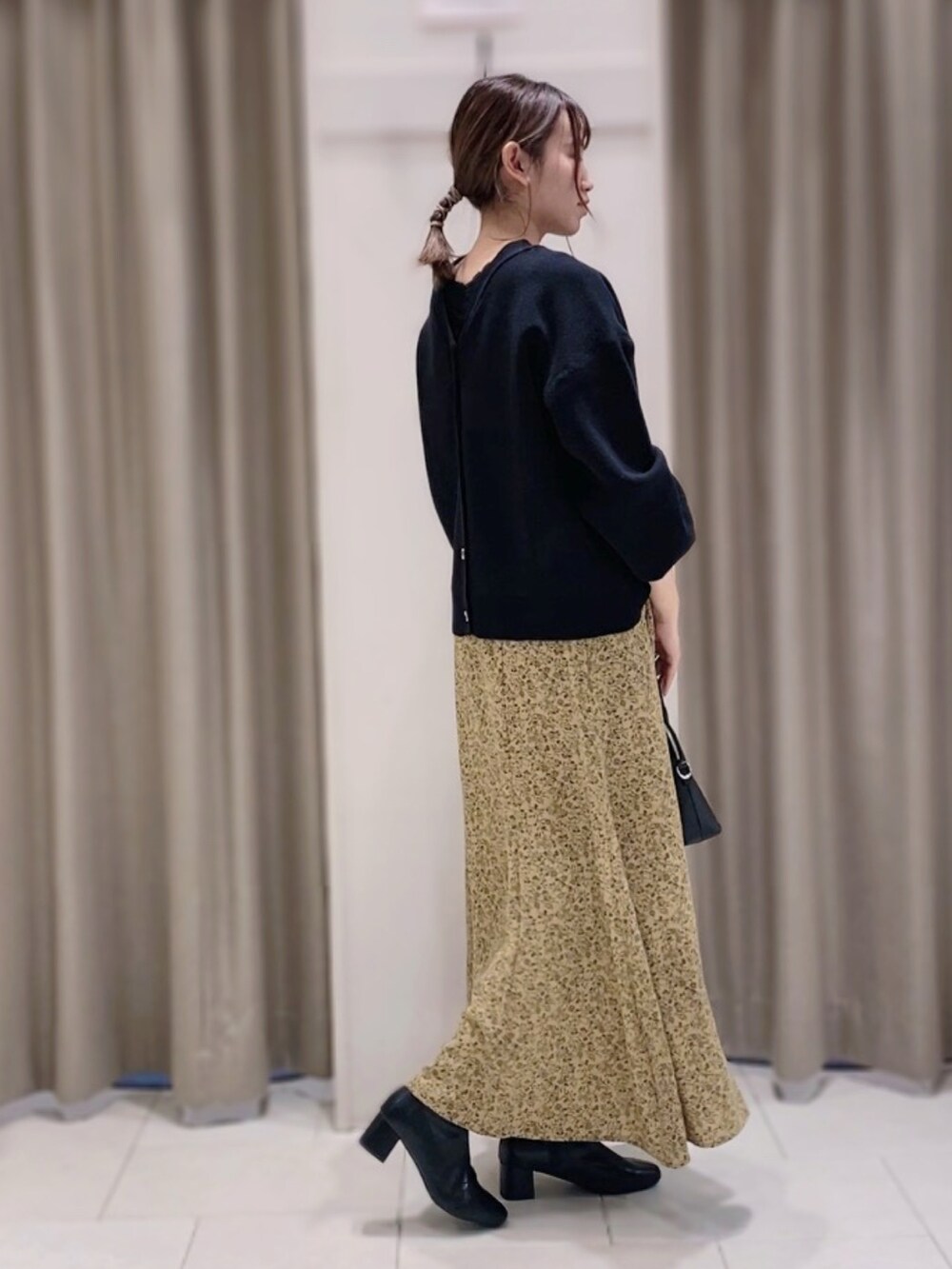 ブラック系のトップス、ブラック系のボストンバッグ、イエロー系のスカートを着用したレディースの秋コーディネートの2枚目の写真