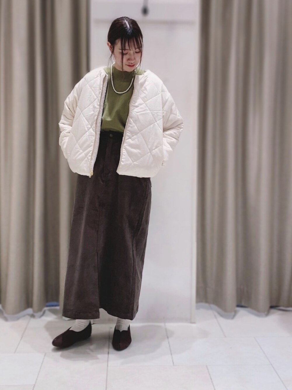 グリーン系のニット/セーター、ホワイト系のブルゾン、ブラウン系のスカートを着用したレディースの秋コーディネートの2枚目の写真