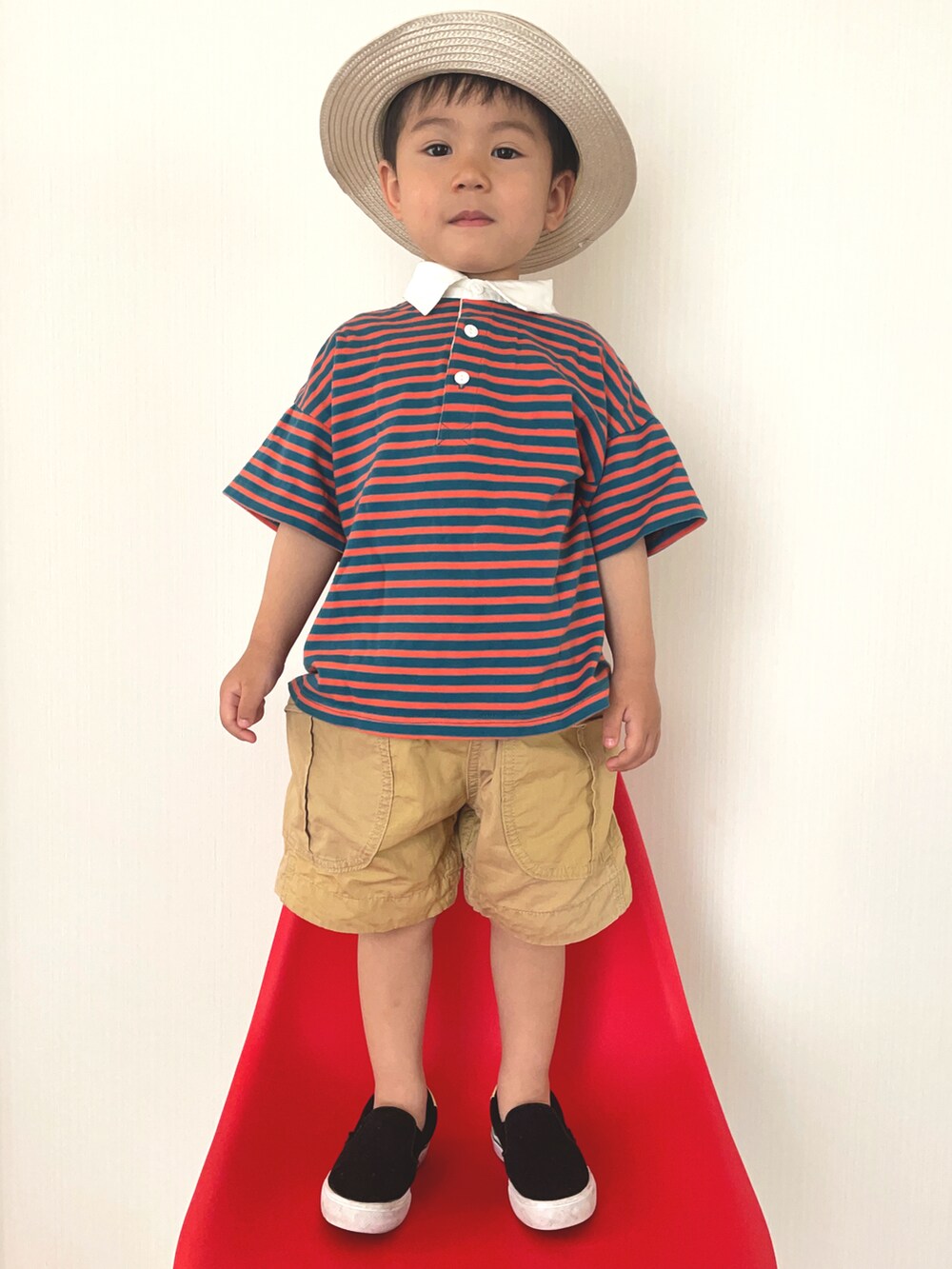 オレンジ系のポロシャツ、ブラック系のスニーカー、ベージュ系のその他パンツを着用したキッズの夏コーディネートの2枚目の写真