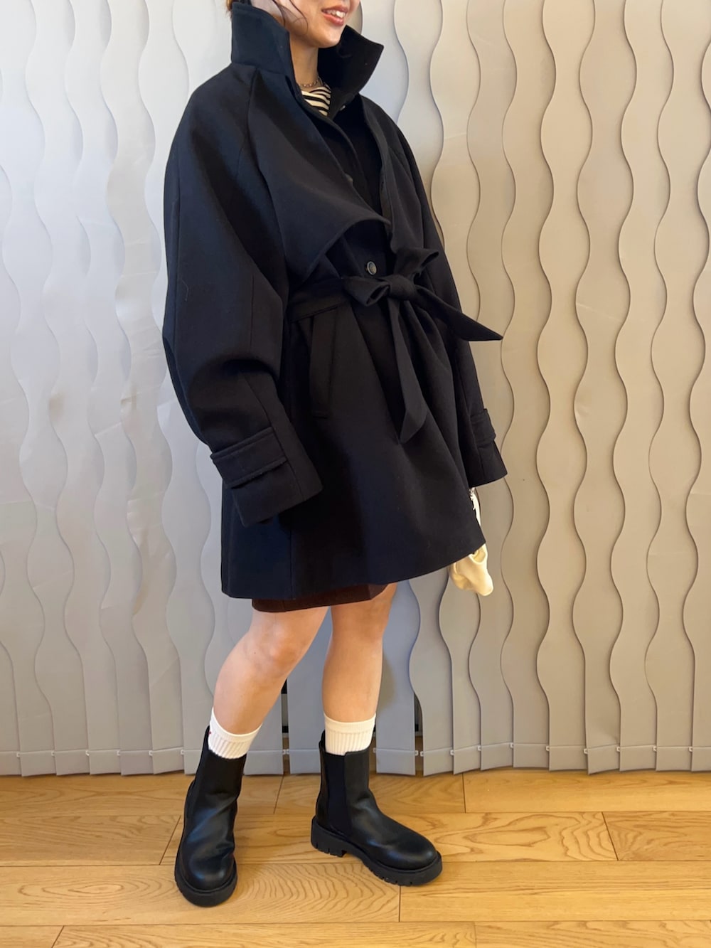 ブラック系のトレンチコート、ブラック系のブーツ、ホワイト系のハンドバッグを着用したレディースの秋コーディネートの3枚目の写真