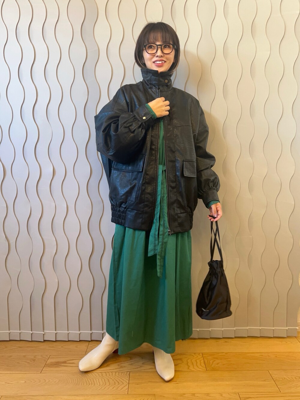 ブラック系のブルゾン、ホワイト系のブーツ、グリーン系のワンピースを着用したレディースの秋コーディネートの2枚目の写真