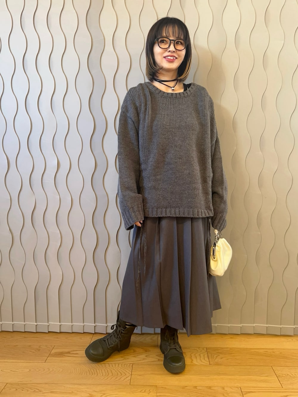 グレー系のニット/セーター、グレー系のスカート、ホワイト系のハンドバッグを着用したレディースの秋コーディネートの2枚目の写真