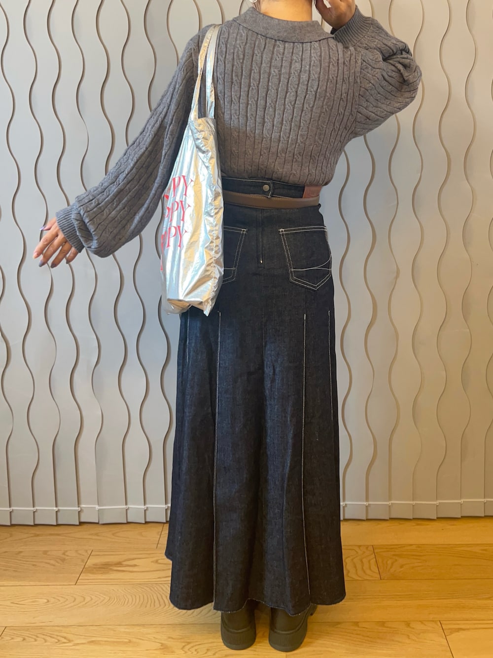 グレー系のニット/セーター、シルバー系のトートバッグ、ブルー系のデニムスカートを着用したレディースの秋コーディネートの2枚目の写真