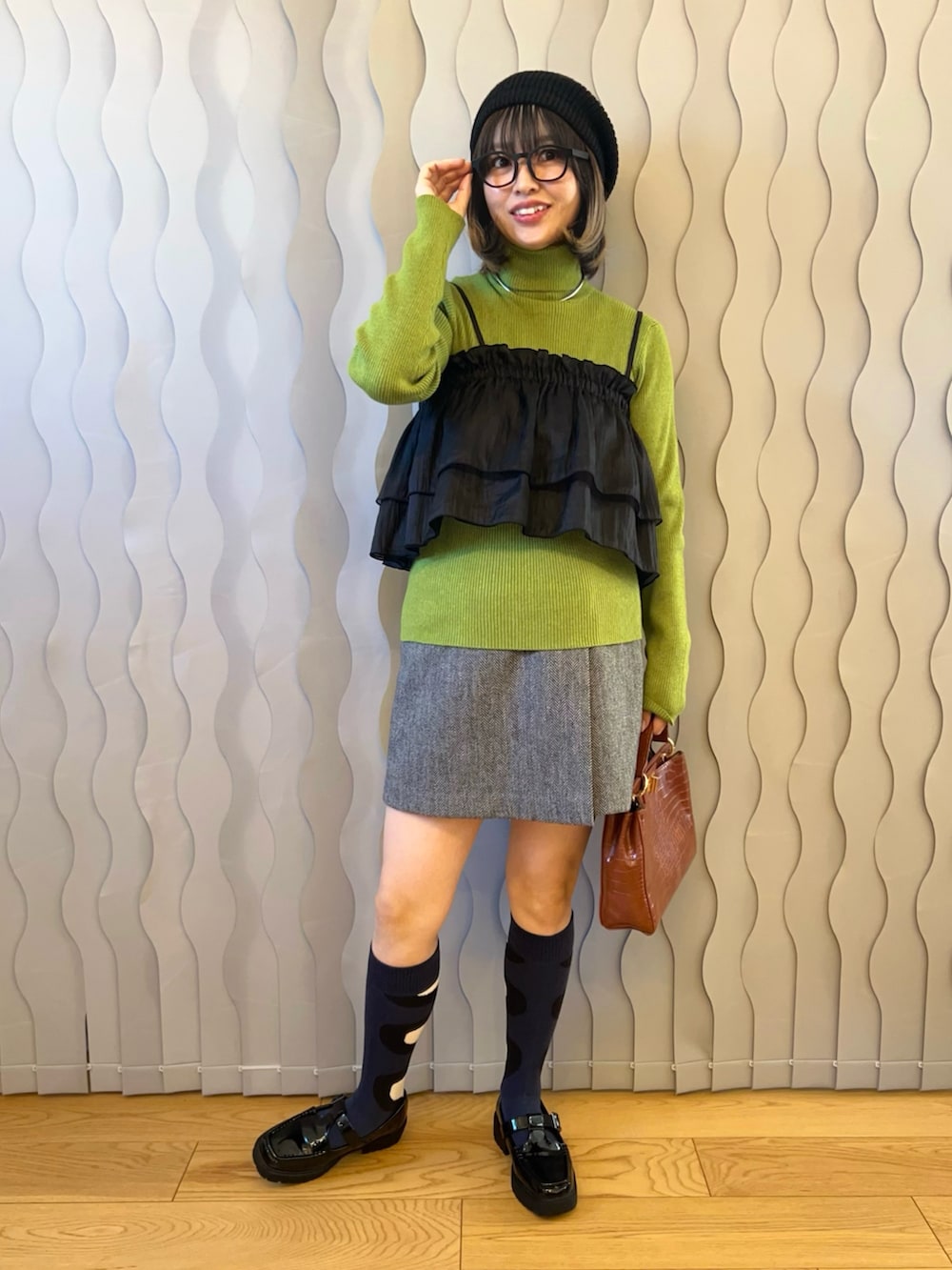 グリーン系のニット/セーター、ブラック系のキャミソール、ブラウン系のハンドバッグを着用したレディースの秋コーディネートの2枚目の写真
