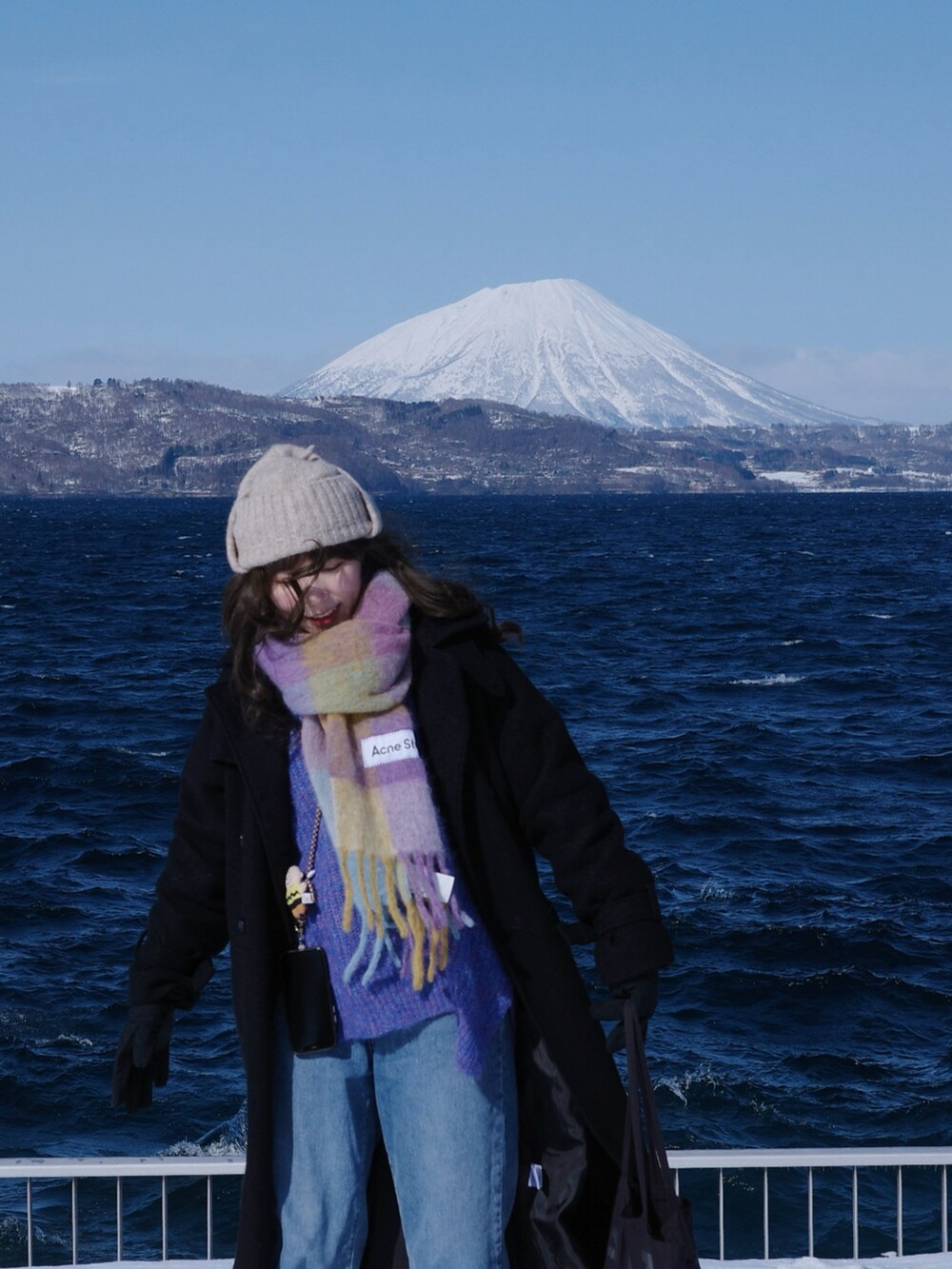 パープル系のニット/セーター、ブラック系のチェスターコート、ブラウン系のスリッポンを着用したレディースの冬コーディネートの2枚目の写真