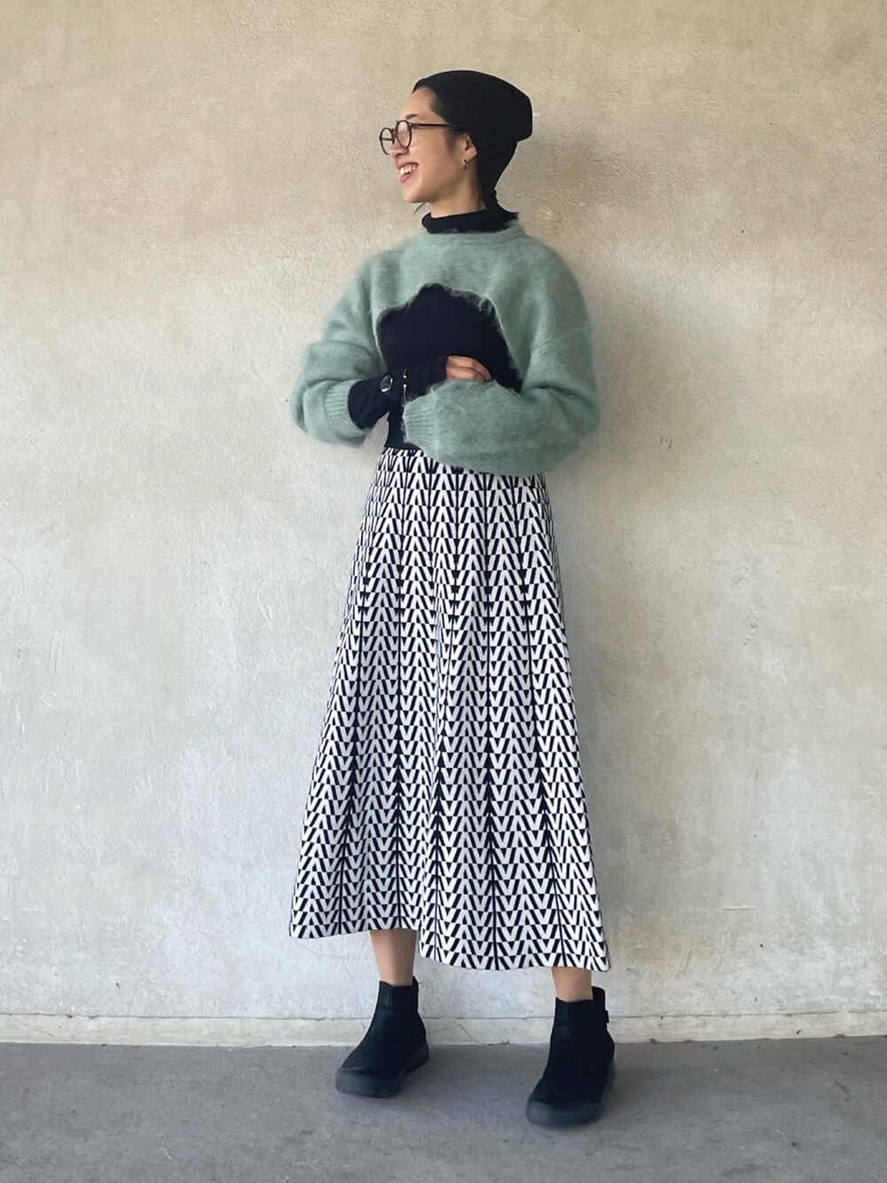 グリーン系のニット/セーター、ホワイト系のスカート、ブラック系のブーツを着用したレディースの冬コーディネートの5枚目の写真