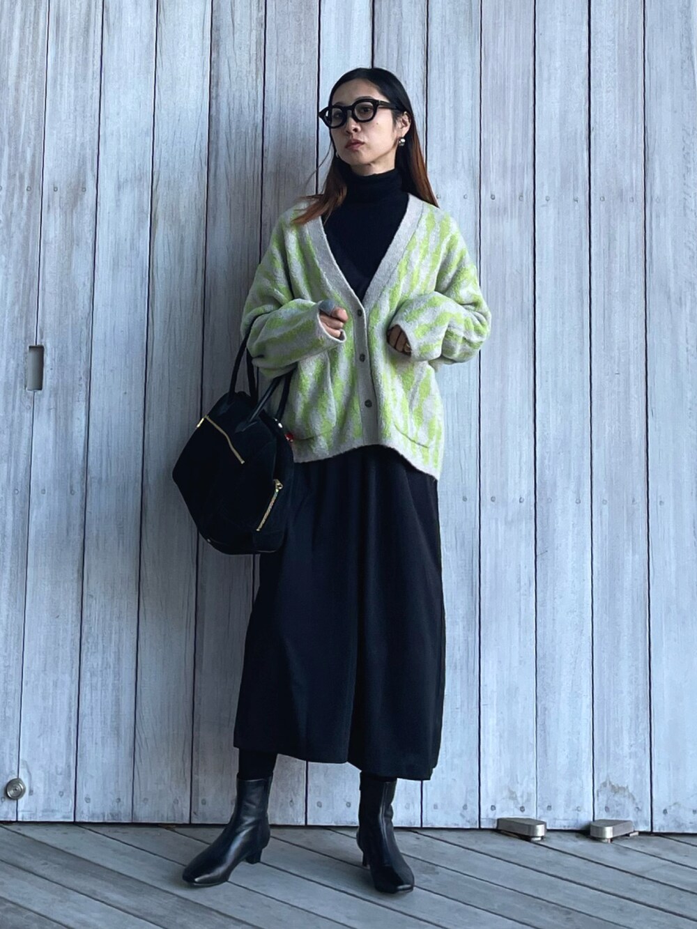 グリーン系のカーディガン/ボレロ、ブラック系のブーツ、ブラック系のサロペット/オーバーオールを着用したレディースの秋コーディネートの2枚目の写真