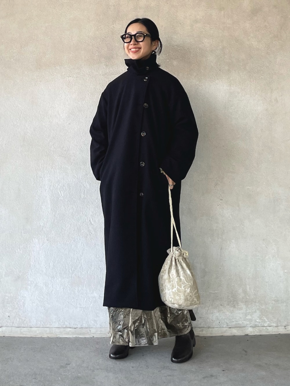 ブラック系のステンカラーコート、グリーン系のニット/セーター、シルバー系のスカートを着用したレディースの冬コーディネートの2枚目の写真