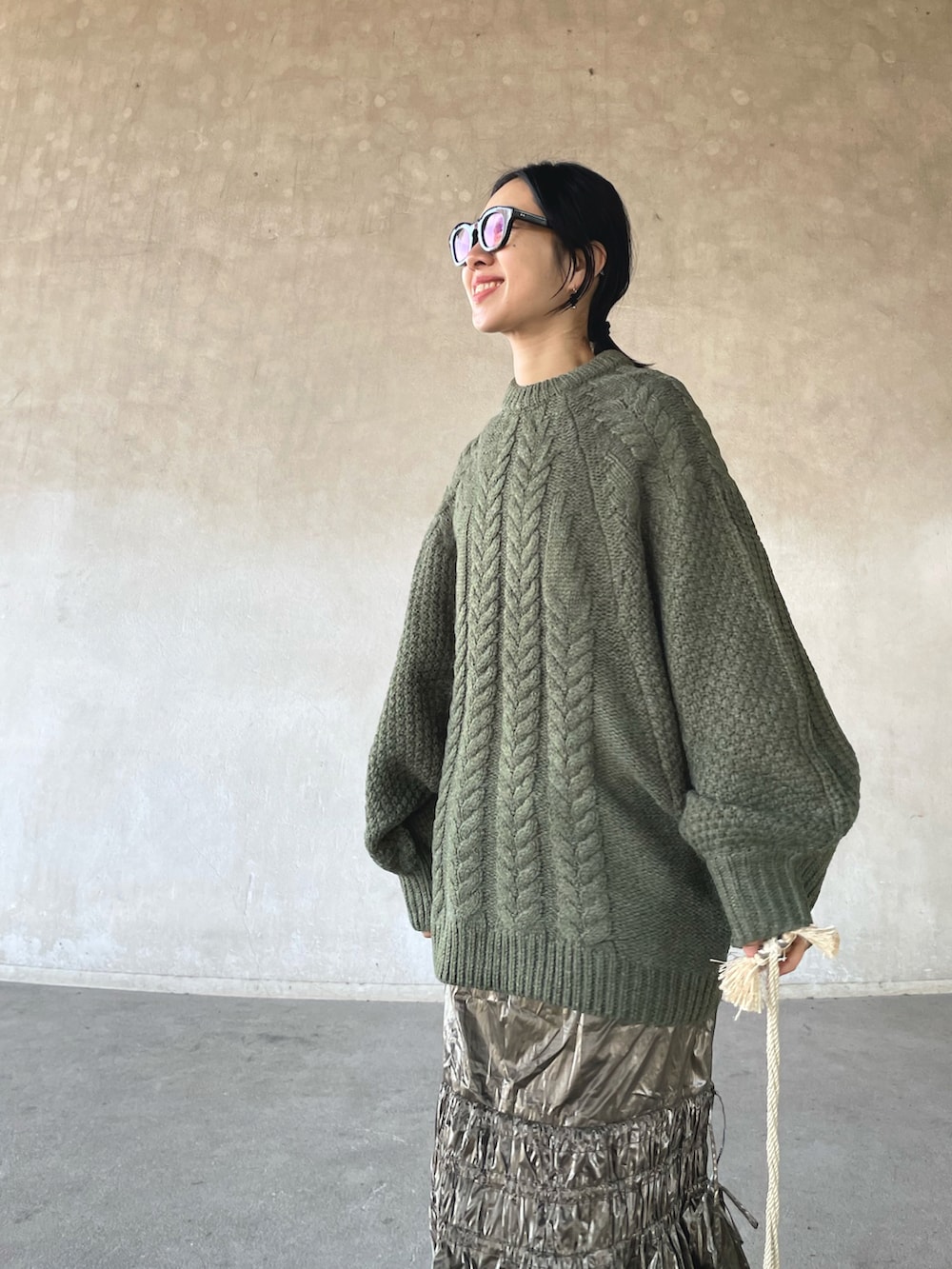 ブラック系のステンカラーコート、グリーン系のニット/セーター、シルバー系のスカートを着用したレディースの冬コーディネートの5枚目の写真