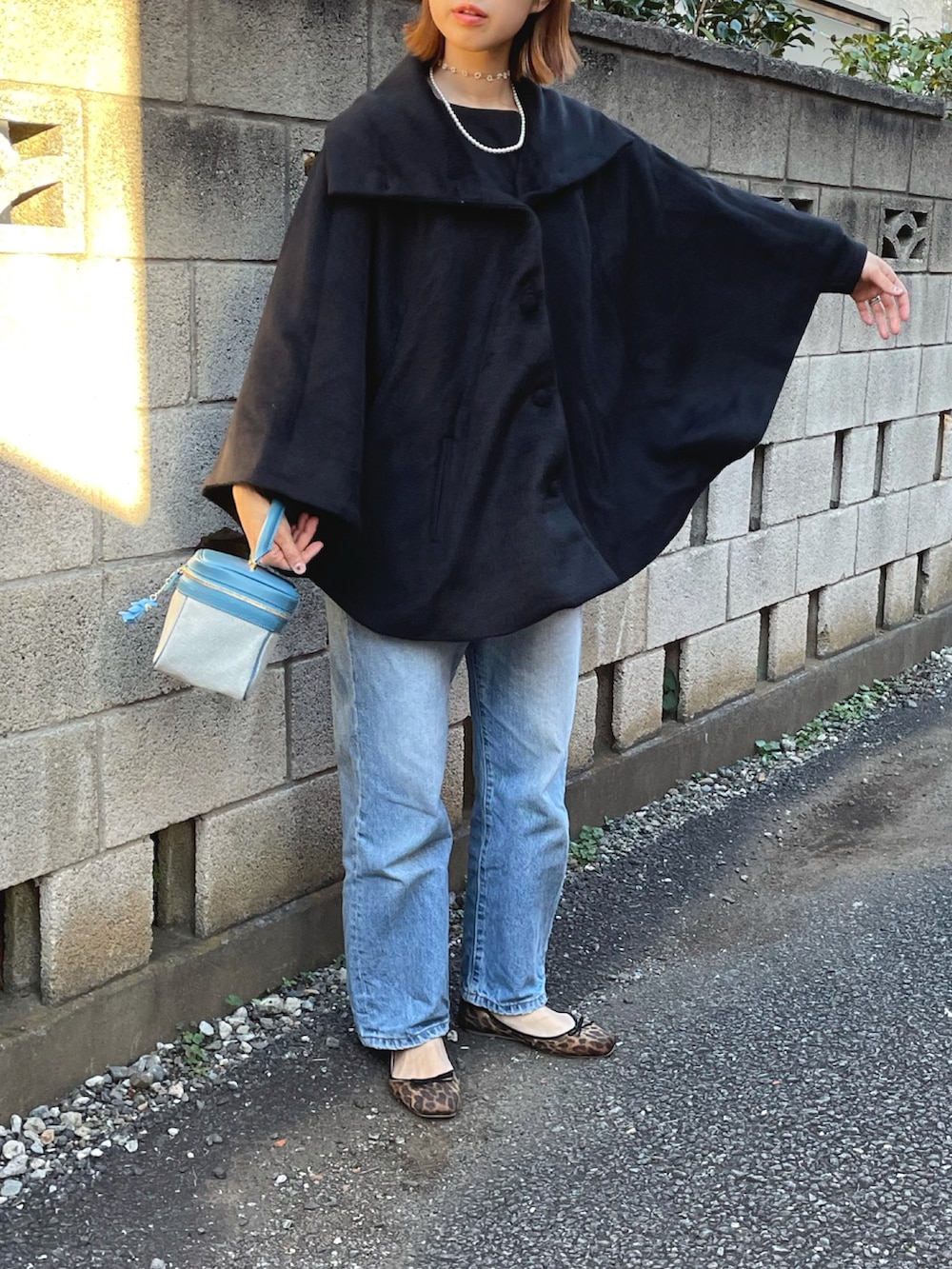 ブラック系のポンチョ、ブルー系のハンドバッグ、ブルー系のデニムパンツを着用したレディースの秋コーディネートの3枚目の写真