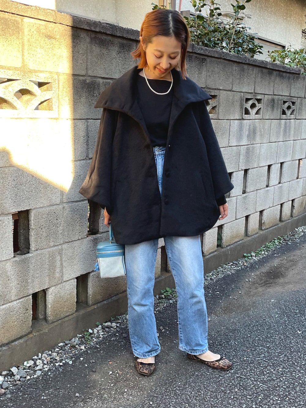 ブラック系のポンチョ、ブルー系のハンドバッグ、ブルー系のデニムパンツを着用したレディースの秋コーディネートの4枚目の写真