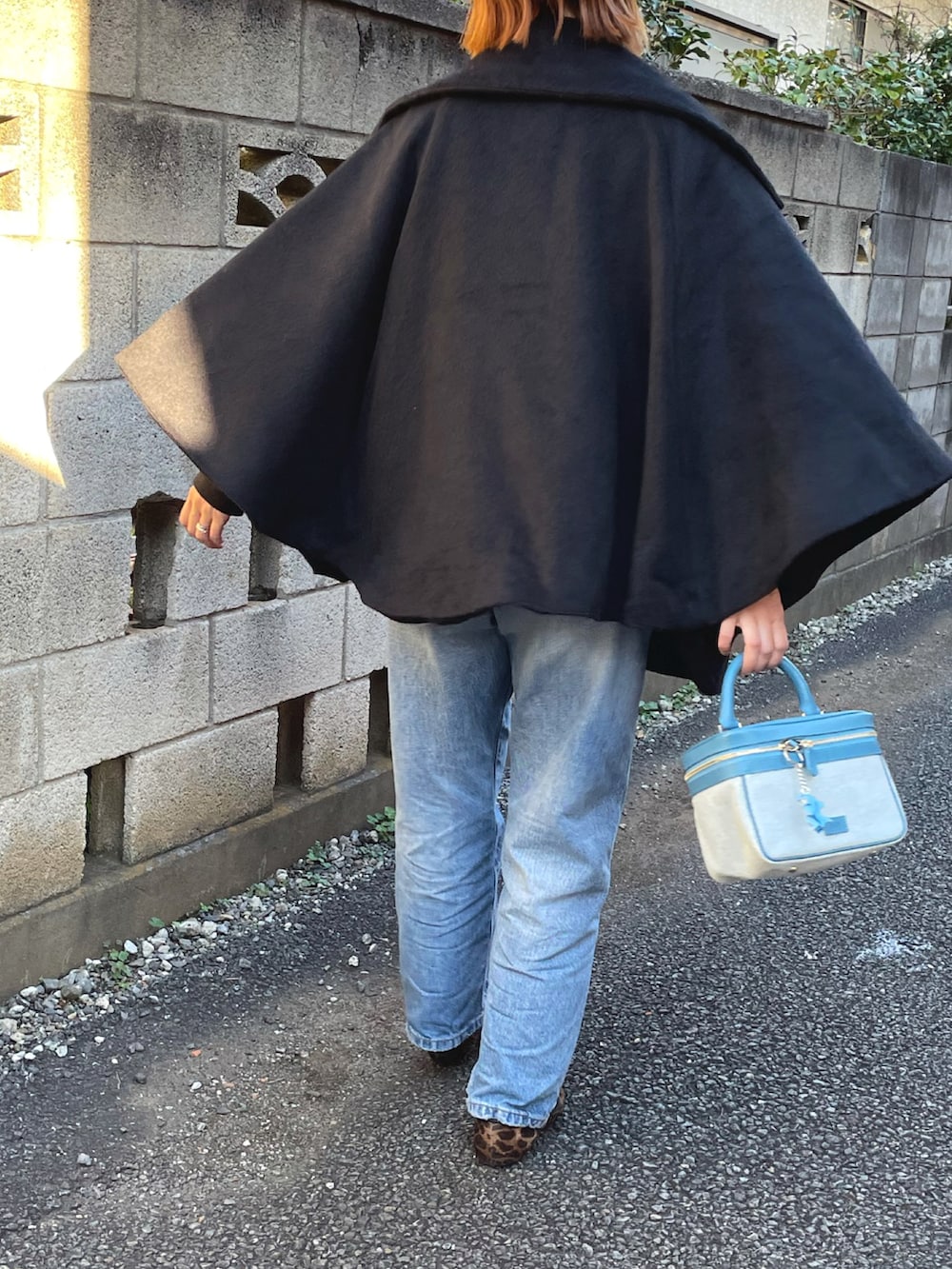 ブラック系のポンチョ、ブルー系のハンドバッグ、ブルー系のデニムパンツを着用したレディースの秋コーディネートの2枚目の写真