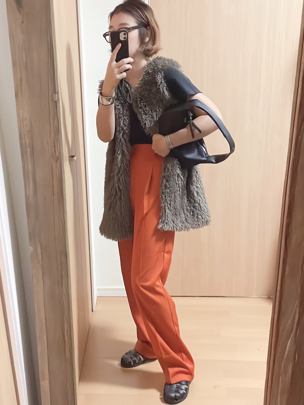 グレー系のベスト、オレンジ系のスラックス、ブラック系のサンダルを着用したレディースの夏コーディネートの2枚目の写真