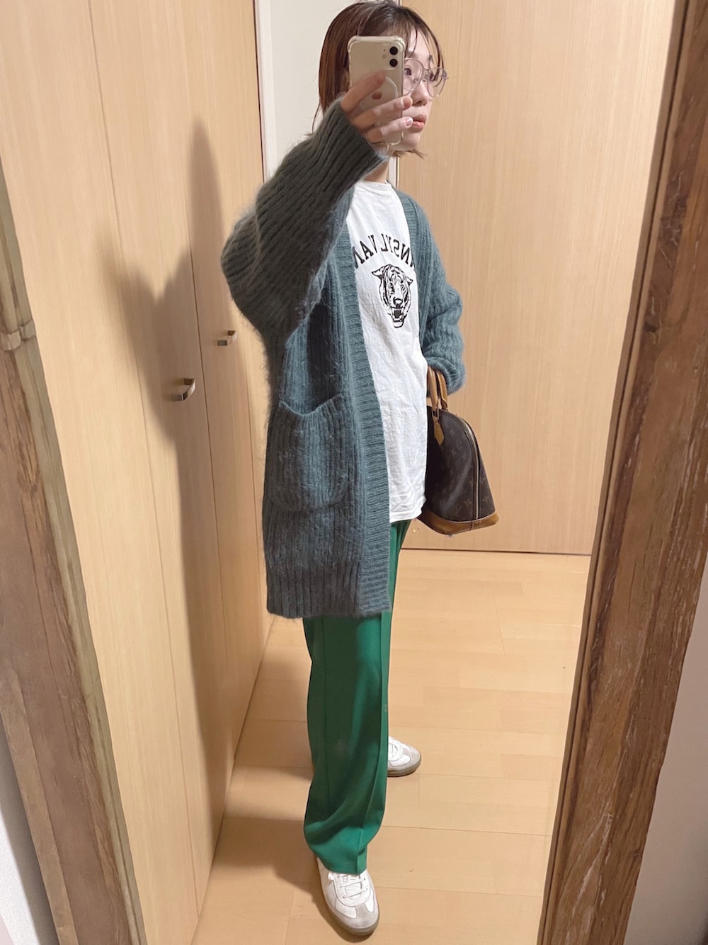 ブラウン系のボストンバッグ、ホワイト系のTシャツ/カットソー、グリーン系のカーディガン/ボレロを着用したレディースの冬コーディネートの2枚目の写真