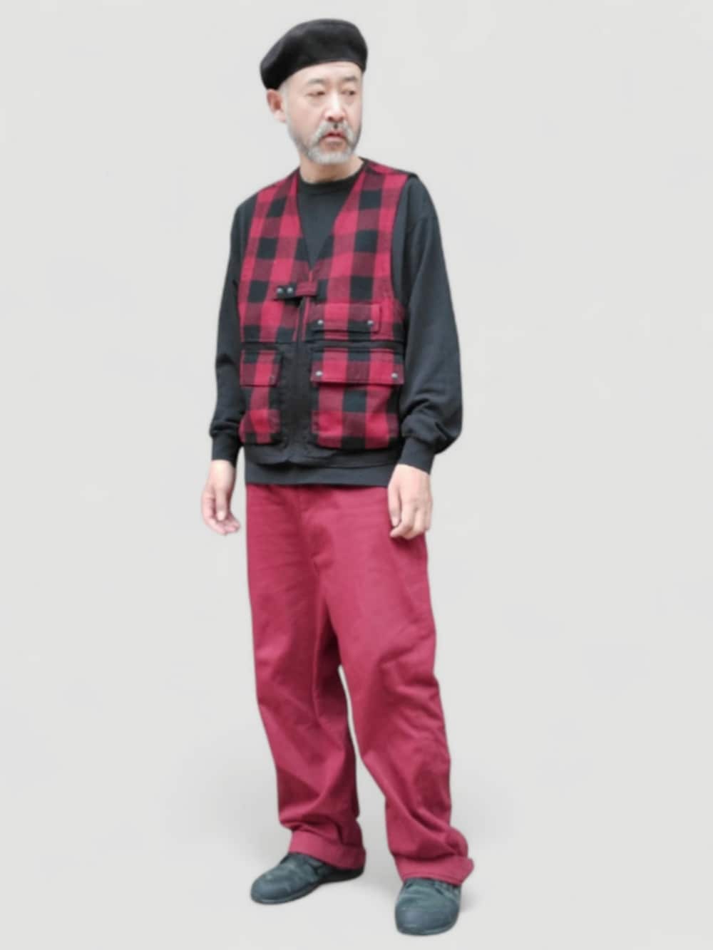 レッド系のチノパンツ、レッド系のベスト、ブラック系のスニーカーを着用したメンズの秋コーディネートの3枚目の写真