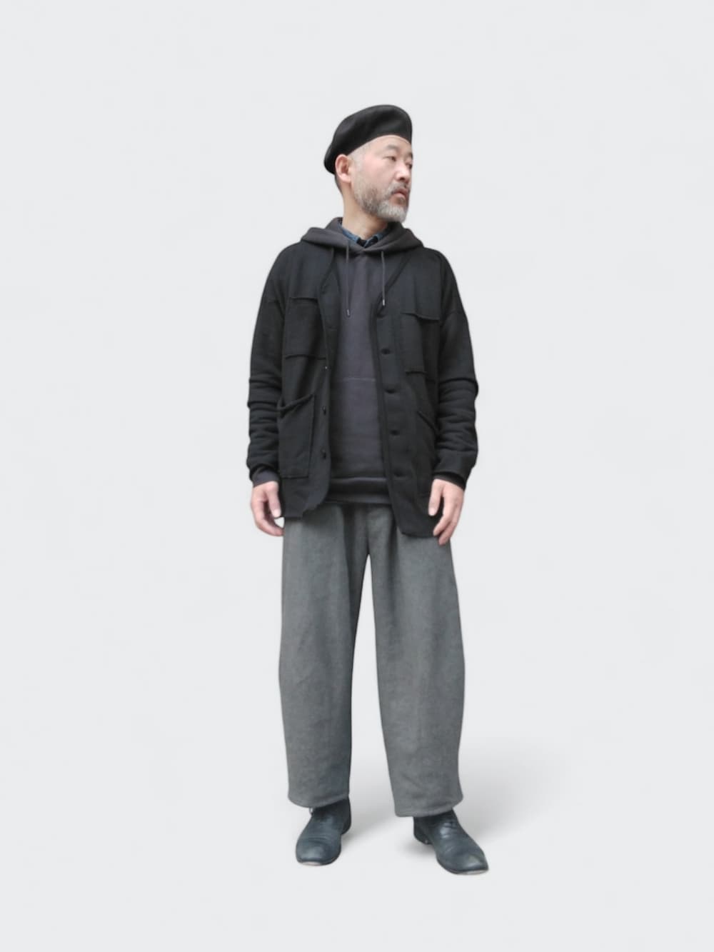 グレー系のパンツ、ブラック系のカーディガン/ボレロ、ブラック系のハンチング/ベレー帽を着用したメンズの春コーディネートの2枚目の写真