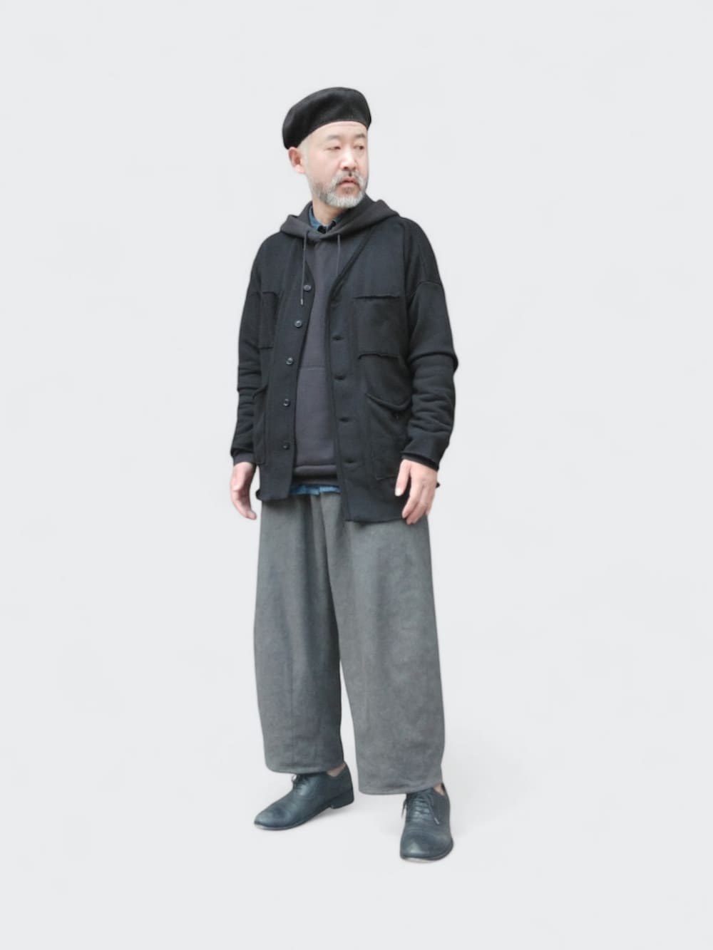 グレー系のパンツ、ブラック系のカーディガン/ボレロ、ブラック系のハンチング/ベレー帽を着用したメンズの春コーディネートの3枚目の写真