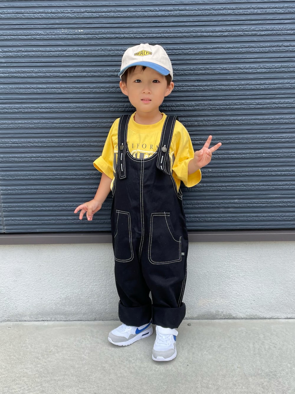 イエロー系のTシャツ/カットソー、ブラック系のサロペット/オーバーオール、ホワイト系のスニーカーを着用したキッズの秋コーディネートの2枚目の写真