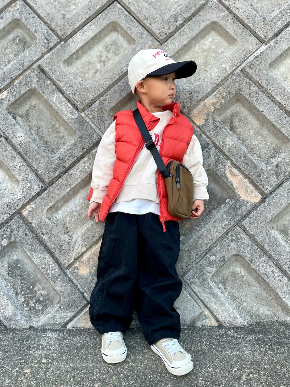 オレンジ系のダウンベスト、ベージュ系のスウェット、ブラウン系のショルダーバッグを着用したキッズの秋コーディネートの3枚目の写真