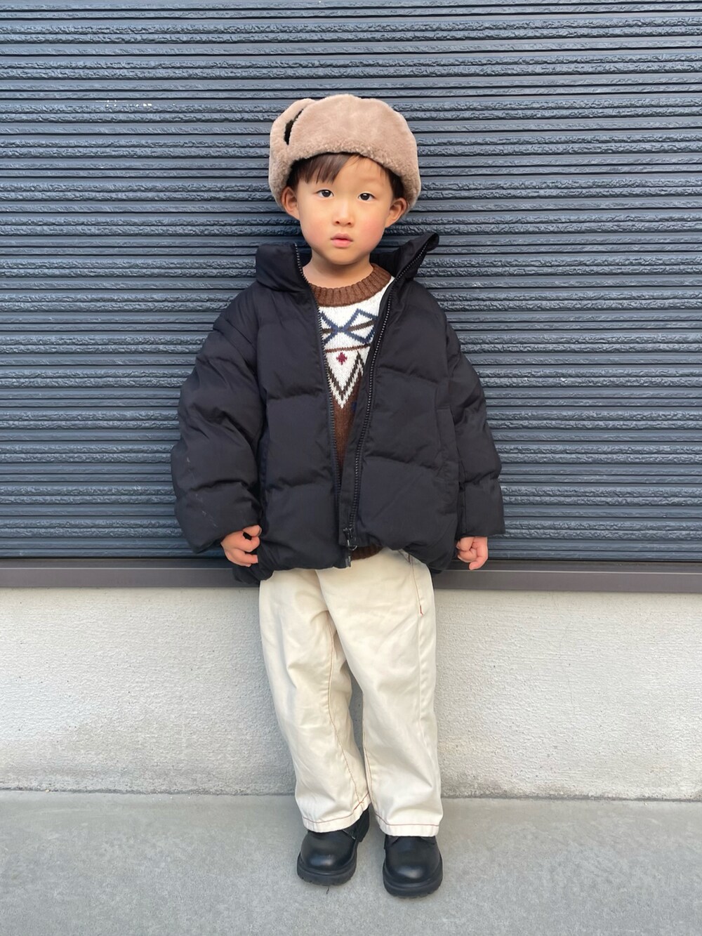 ブラウン系のニット/セーター、ブラック系のブルゾン、ホワイト系のデニムパンツを着用したキッズの冬コーディネートの2枚目の写真