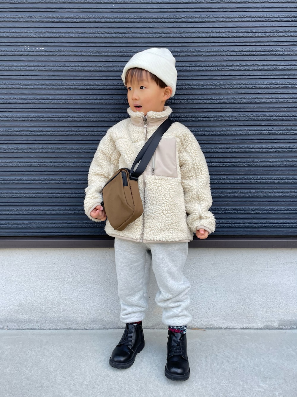 ブラウン系のショルダーバッグ、ベージュ系のその他アウター、グレー系のスウェットパンツを着用したキッズの冬コーディネートの2枚目の写真