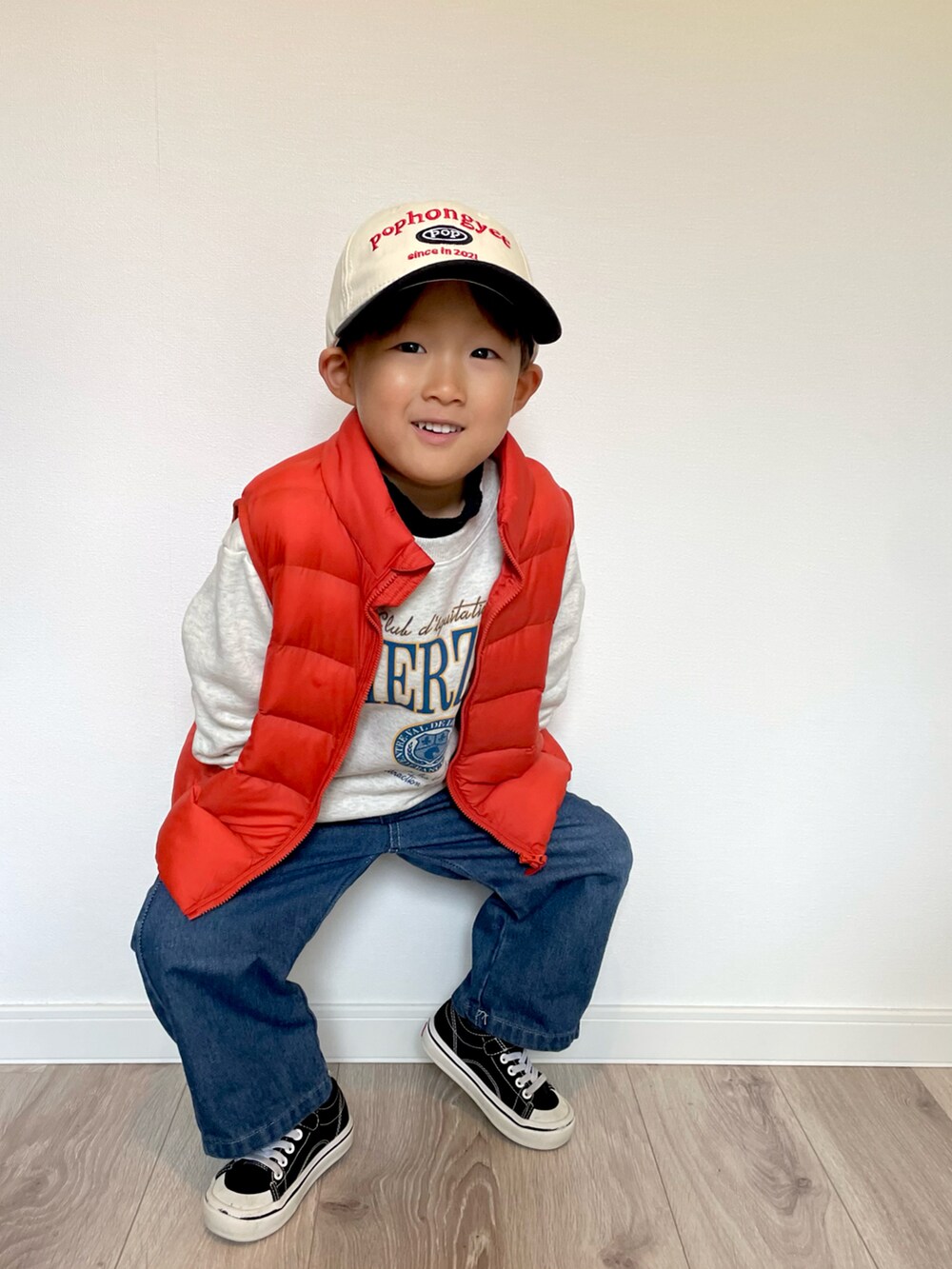 オレンジ系のダウンベスト、グレー系のスウェット、ブルー系のデニムパンツを着用したキッズの冬コーディネートの3枚目の写真