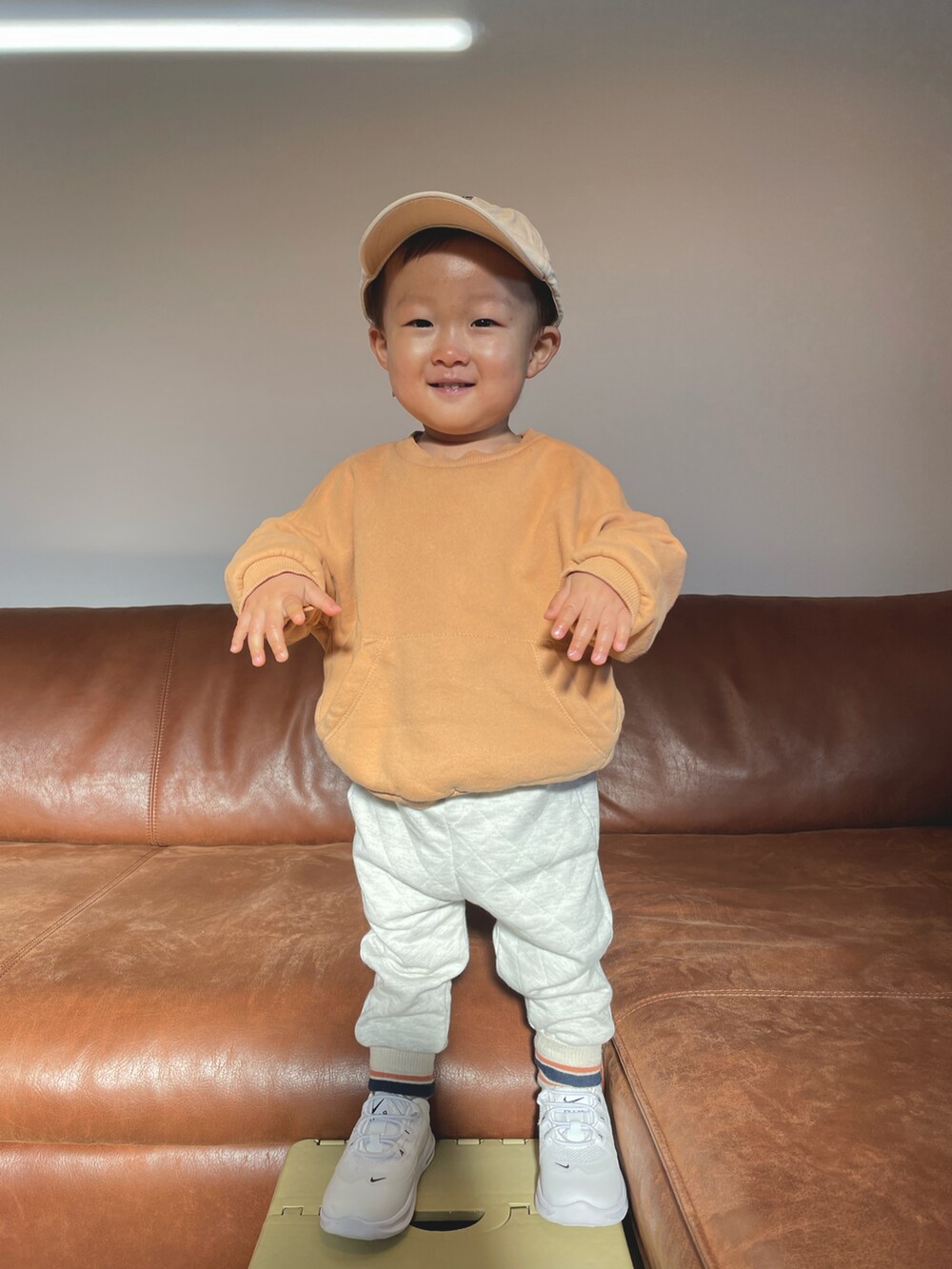 オレンジ系のスウェット、ホワイト系のその他パンツ、ベージュ系のキャップを着用したキッズの冬コーディネートの2枚目の写真