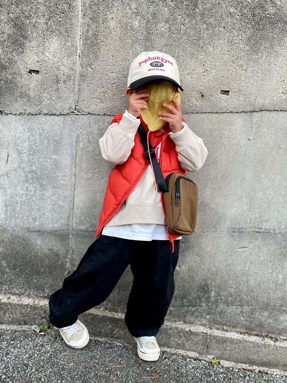オレンジ系のダウンベスト、ベージュ系のスウェット、ブラウン系のショルダーバッグを着用したキッズの秋コーディネートの5枚目の写真