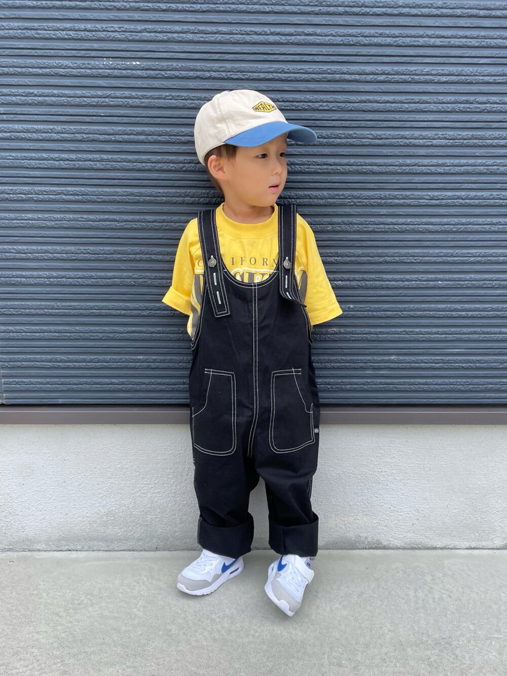 イエロー系のTシャツ/カットソー、ブラック系のサロペット/オーバーオール、ホワイト系のスニーカーを着用したキッズの秋コーディネートの3枚目の写真